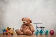 Retro plush Teddy Bear, old toy trike bicycle, obsolete wooden truck with construction blocks and leather ball front concrete textured wall background. Vintage style filtered photo