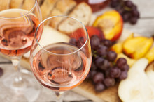 Two Glasses Of Rose Wine And Board With Fruits, Bread And Cheese On Wooden Table, Shallow DOF