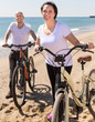 © caftor - middle-aged man and woman with bicycles walking on the beach