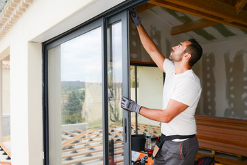 Wall Mural - handsome young man installing bay window in a new house construction site