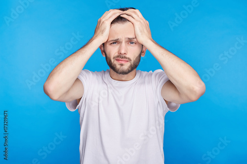 Fotografie, Obraz Portrait of forgetful young European or American customer or employee wearing white t-shirt looking with shocked and guilty expression, holding hands on his head, opening mouth widely