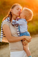 Wall Mural - Woman and child outdoors at sunset. Boy kissing his mom.