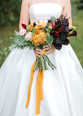 style, floral arranging, wedding concept. young woman dressed in extremely beautiful snowy white dress with puffy skirt is holding great bunch of different flowers stretched with yellow ribbons