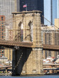 Brooklyn Bridge Tower with USA flag, Manhattan buildings background early in the morning with blue sky and sun shine - Brooklyn, New York, NY, United States of America, USA