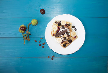 A photo of two Viennese wafers, poured with chocolate with berries and ice cream on a wooden table on the boards. chestnuts, tea, jam, autumn