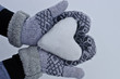women's hands in cozy warm mittens keep the heart out of the snow against the background of snow