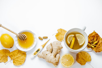 Tea with lemon, thermometer, ginger, honey, tablets and dry leaves on a white background. top view, flat lay, space for text.