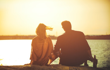 Wall Mural - Happy couple sitting at the beach during sunset, love and friendship