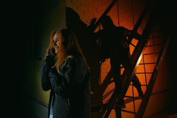 Criminal stalking a girl alone in a dark street. He is hiding in the shadows and the woman is alone on the street.