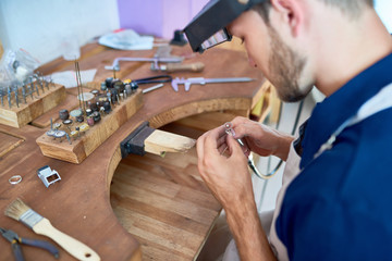 Wall Mural - Portrait of craftsman making jewelry in workshop, forming and polishing it on work station with different tools