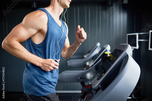 Fotografia Unrecognizable muscular man in headphones enjoying favorite song while running o