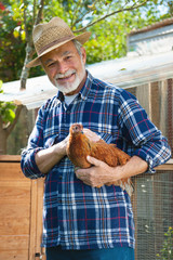 Farmer holds chicken in his arms in front of hen house