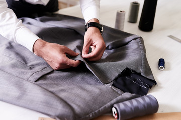 Production process of custom-made male jacket: unrecognizable tailor concentrated on sewing with needle and thread, close-up shot