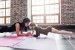 © undrey - Mother and daughter standing in dolphin plank pose, phalankasana, during yoga session in fitness center