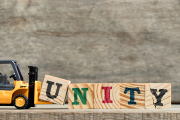 Sticker - Yellow plastic forklift hold letter U to complete word unity on wood background