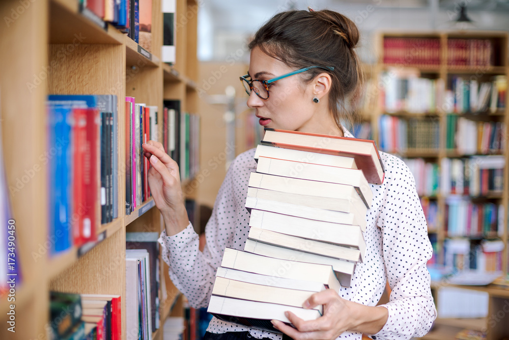 Young woman with a stack of books in library want more Stock Photo ...