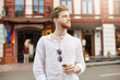 © Cookie Studio - Handsome redhead bearded man with stylish haircut in white shirt walking around city and drinking coffee in morning before hard day on work.