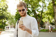 © Cookie Studio - Close up of beautiful ginger male with beard and earring in stylish glasses texting with friend, going home after hard day on work.