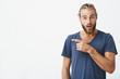 © Cookie Studio - Close up of attractive swedish guy with good hair and beard looking in camera with surprised expression pointing at white wall. Copy space.