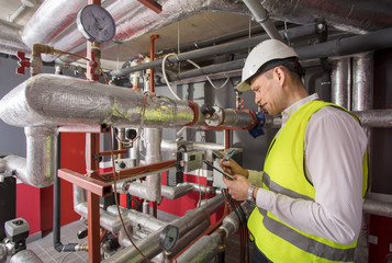 Man in helmet writing down measurements in heat and airconditioning system panel