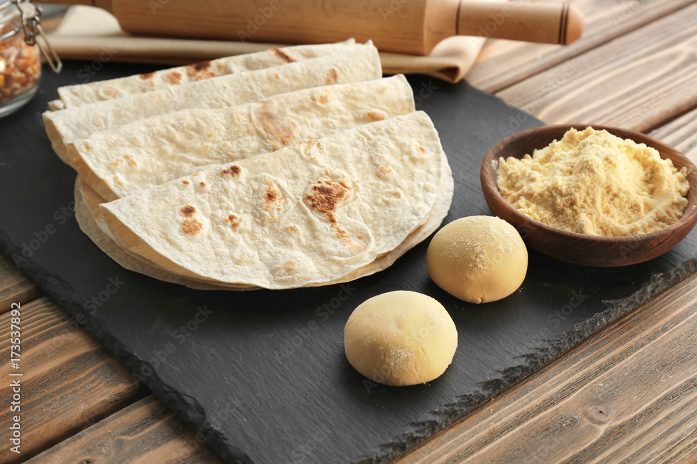 Slate plate with delicious tortillas on wooden table