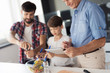 © VadimGuzhva - The old man is looking at something on the tablet, while behind him the boy and man are finishing the salad preparation