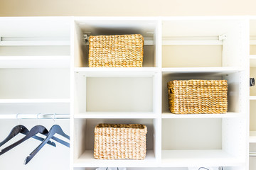 Closeup of woven straw baskets in modern minimalist white closet or laundry room with bright light in staging model house or apartment with hangers