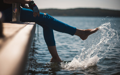 Poster - A happy young girl is kicking feet on a sea pier and splashing water