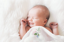 Sleeping Smiling Newborn Baby In A Wrap On White Blanket.