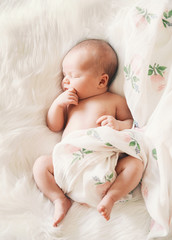 sleeping newborn baby in a wrap on white blanket.