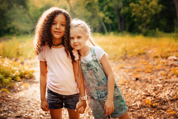 Two happy girls as friends hug each other in cheerful way. Little girlfriends in park.