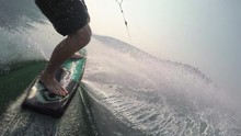 Man Holding Action Camera On Wake Skate Board Towed Behind Boat