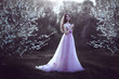 Beautiful Romantic Girl with long hair in pink dress near flowering tree.