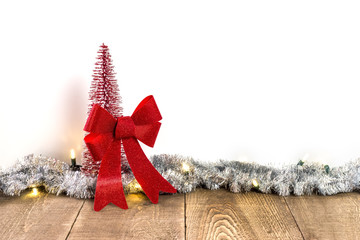 Wall Mural - Small sparkly red Christmas tree and big tied bow on rustic wooden table with light and tinsel