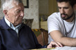 © Jovana Milanko/Stocksy - Grandfather and his grown up grandson sitting and having a conversation inside the living room