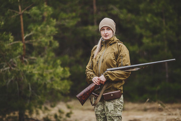 female hunter in camouflage clothes ready to hunt, holding gun and walking in forest.