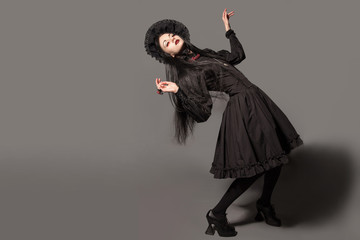 Portrait of brunette woman in black dress and classic gothic style with red eyes on gray background. halloween concept.