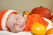 Cute sleeping newborn baby  in a knitted pumpkin or orange costume on pumpkin and oranges background. Autumn halloween or harvest concept.
