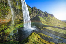 Tourist Standing In Front Of Seljalandsfoss With Rainbow Around , Beautiful Amazing Landscape From Iceland,