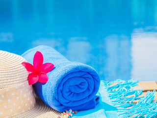 Wall Mural - Red frangipani (plumeria) flowers, sunglasses, beach hat and blue towel at the side of swimming pool. Vacation, beach, summer travel concept