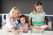 © VadimGuzhva - A woman with a recipe book helps a girl and her grandmother prepare a cake