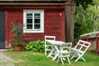 White wooden outdoor furniture outside a red traditional barn window. Flowerpot and flowerbed outside barn.