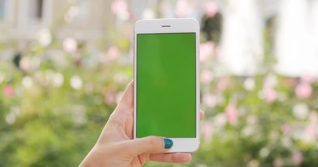 Woman hand holding using mobile smart phone blurred background plants garden green screen chromakey digital display closeup outdoor modern trendy lifestyle device hipster vertical keeping public space