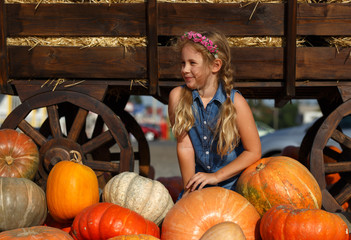 happy school girl sitting between pumpkins at local farmer market in sunny autumn day.