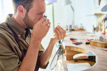 Wall Mural - Side view portrait of jeweler inspecting ring through magnifying glass in workshop