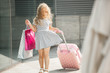 © olenachukhil - Cute little girl holding a shopping bags and suitcase and smiling. Cheerful child preparing for the trip