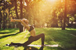 © sandsun - Beautiful young woman practices yoga asana Virabhadrasana 1 - warrior pose 1 in the park at sunset