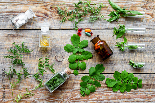 Plakat Medycyna ziołowa. Liście, butelki, pigułki na drewniane tło widok z góry
