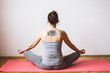 © Aleksandra Jankovic/Stocksy - Back view of a tattooed woman meditating in the lotus position