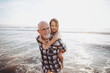 © Rob and Julia Campbell/Stocksy - Fun, energetic grandpa playing in waves with young grandchild - girl - on beach at sunset - shoulder ride
